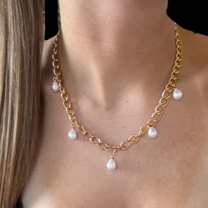 Pärlhalsband Guld - Stilrent halsband i guldton med chunky kedja och fem droppformade vita pärlor som hänger längs länkarna. Perfekt för dig som vill ha en elegant och trendig accessoar som sticker ut och ger extra glans till din look.
