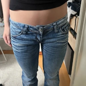 Lågmidjade bootcut jeans - Säljer ett par ljusblå jeans med broderade detaljer på bakfickorna. Jeansen har låg midja och utsvängda ben. Storlek W29/L32 Midjan är 39cm tvärsöver och innerbenslängden är 80cm