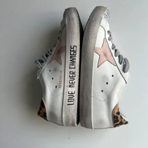 Golden Goose sneakers TYP ALDRIG ANVÄNDA! - Golden Goose sneakers i vitt skinn med ljusrosa stjärna på sidan, grå snörning och texten 'LOVE NEVER CHANGES' på sulan. Tåpartiet har silverglittrig detalj och hälen är klädd i leopardmönstrad päls. Snygg mix av material och coola detaljer.