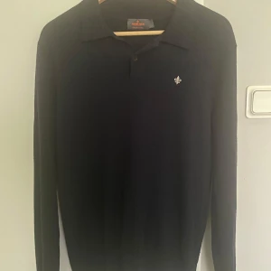 Mörkblå Morris Merinoull Tröja  - Snygg mörkblå tröja från Morris i 100% merinoull. Tröjan har klassisk krage, knappar vid halsen och en broderad logga på bröstet.                   Pris kan diskuteras!