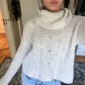 Ljusgrå stickad polotröja - Supermysig ljusgrå stickad polotröja med grov kabelstickning och bred krage. Tröjan har lång ärm och en loose passform som ger en chill vibe. Perfekt att matcha med jeans för en enkel och snygg look. Materialet är mjukt och värmande, perfekt för kyliga dagar.