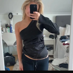 Svart oneshoulder topp  - Säljer en svart oneshoulder topp med lång ärm på ena sidan. Toppen har en tajt passform som framhäver figuren på ett väldigt fint sätt!