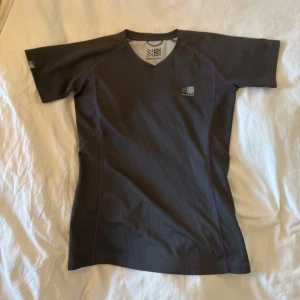 Svart tränings-tshirt från Karrimor - Sportig svart t-shirt från Karrimor med lila sömmar och diskret logga på bröstet. T-shirten har korta ärmar, v-ringad hals och är gjord i ett lätt syntetmaterial som andas. Perfekt för gymmet eller löprundan.