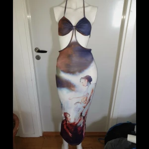 Lång omlottklänning med konsttryck - Supersnygg lång klänning med konstnärligt tryck i blått, brunt och vitt. Halterneck med knyt i nacken och öppen rygg, omlott-design framtill. Tight passform och mjukt, stretchigt material som känns som polyester. 