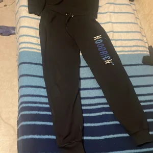 Svart hoodie från Hoodrich med blått tryck - Svart hoodie från Hoodrich med stort blått och vitt tryck på bröstet. Tröjan har huva med snörning, känguruficka och långa ärmar. Materialet är mjuk bomull och passformen är normal. Perfekt för dig som gillar streetwear och vill sticka ut med snyggt tryck. Själv är jag 1,73 och den passar fortfarande bra