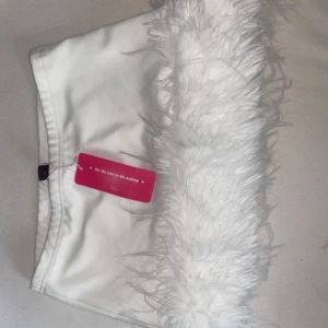 Vit kjol med fluffig pälsdetalj - Supersnygg vit kortkjol med en bred, fluffig pälsdetalj längs nederkanten. Kjolen har en clean och modern look, perfekt för dig som vill sticka ut med en unik och trendig stil. Passar dig som gillar statement-plagg och att mixa texturer.