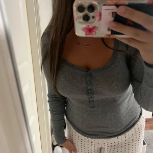 Grå ribbad långärmad tröja Victoria's Secret - Superskön grå långärmad tröja från Victoria's Secret med ribbad struktur och snygga knappar framtill. Tröjan har en rundad halsringning och sitter tight mot kroppen, perfekt för chill eller när du vill ha en enkel men stilren look.