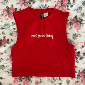 Röd croppad topp - Röd croppad linnetopp från H&M i strl XS med vit broderad text 'not your baby' på bröstet. Toppen är ärmlös och har en rund halsringning!💞