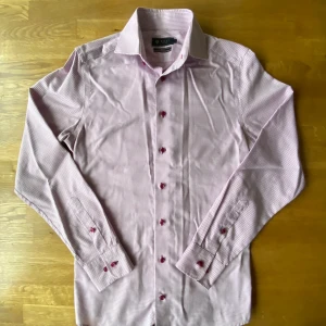Rutig rosa skjorta Riley slim fit - Snygg rosa och vit rutig skjorta från Riley i slim fit-modell. Skjortan har långa ärmar, klassisk krage och rosa knappar som ger en schysst detalj. Perfekt för dig som gillar stilrena och moderna plagg med lite edge.