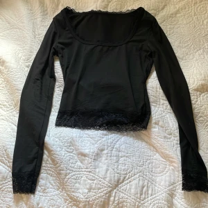 Svart långärmad spetsblus från SHEIN - En oanvänd supersnygg svart blus från SHEIN med lång ärm och bred, fyrkantig urringning. Spetsdetaljer vid nederkant och ärmslut ger en extra touch. Tillverkad i mjuk polyester med lite stretch för skön passform. Perfekt för dig som gillar stilrena och feminina plagg.