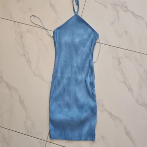 Blå ribbad kort klänning med knyt - Säljer en ljusblå ribbad kortklänning med smala axelband och snygg knytning i nacken. Klänningen är ärmlös och har en tight passform som framhäver figuren. Perfekt för sommarens varma dagar och har en stilren, enkel design.