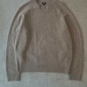 Beige stickad tröja från Uniqlo - Säljer en stilren beige stickad tröja från Uniqlo. Tröjan har rund hals, långa ärmar och ribbade muddar vid ärmslut och nederkant. Perfekt för lager-på-lager och chill dagar. Enkel att matcha med jeans eller chinos.