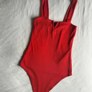 Röd body  - Snygg röd body med breda axelband och en liten v-ringning framtill. Modellen är enkel och stilren, perfekt för dig som vill ha en klassisk look. Materialet känns mjukt och följsamt mot huden.