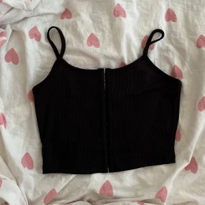 Svart ribbad korsett-topp - En ribbad svart croppad korsett-topp från SHEIN i strl S med smala axelband och hakknäppning framtill!💞