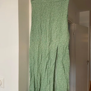 Grön blommig kjol från H&M - Säljer en grön kjol från H&M i storlek 34. Klänningen har ett sött blommigt mönster i vitt. Tight passform med slits och dragkedja i sidan. 
