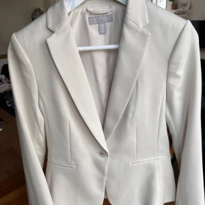 Beige kavaj H&M, strl 34 - Snygg beige kavaj från H&M i storlek 34. Klassisk modell med smal passform, spetsiga slag och en knapp framtill. Kavajen har två fejkfickor och är tillverkad i polyester och viskos. Perfekt för dig som gillar minimalistisk stil. Endast använd ett fåtal gånger och i superfint skick. Är hel o ren. 