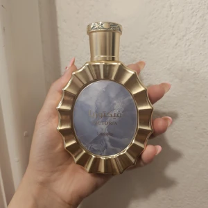 Lattafa Victoria parfym - Lattafa Victoria parfym i en unik, rund guldig flaska med vågformade kanter och ett blåmarmorerat motiv på framsidan. Flaskan har eleganta detaljer och lock med mönster. Perfekt för dig som gillar lyxig design och orientaliska dofter.