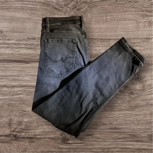 Mörkgrå jeans från Jack & Jones - Säljer ett par snygga mörkgrå jeans från Jack & Jones. De har en klassisk femficksdesign och är i bra skick. Perfekta för både vardag och helg! Passformen är straight och de är tillverkade i ett bekvämt denimtyg.