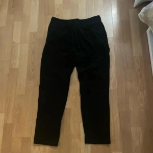 Svarta tygbyxor från Zara - Snygga svarta tygbyxor från Zara med elastisk midja och snörning. Perfekta för en avslappnad stil. Byxorna har en klassisk design och är gjorda i mjukt tyg.