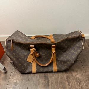 Brun mönstrad resväska ifrån Louis Vuitton 55 - Säljer en stilren brun resväska med ikoniskt mönster och läderdetaljer. Väskan har dubbla handtag och en dragkedja för säker förslutning. Perfekt för resor och weekendutflykter.