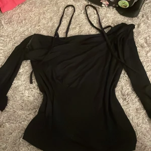 Svart offshoulder topp - Snygg svart offshoulder topp med smala axelband. Perfekt för en stilren look. Toppen har en elegant design som passar till många tillfällen.