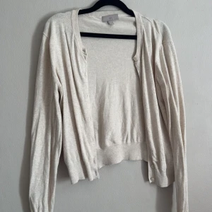 Beige kofta från H&M - Säljer en stilren beige kofta från H&M. Koftan har en klassisk design med knappar framtill och långa ärmar. Perfekt för lager-på-lager under kyligare dagar.