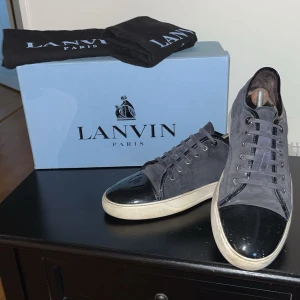 Marinblå sneakers från Lanvin - Snygga marinblå sneakers från Lanvin med svarta detaljer och blå snörning. Skorna har en svart captoe och en vit sula som ger en stilren look. Perfekta för en trendig vardagsstil. Obs det finns en röd fläck på skosnöret som är minimalt. Dustbags samt Skokartong medföljer såklart. Hör av er vid frågor!  Köp direkt för 1300(går inte ner mer i pris)