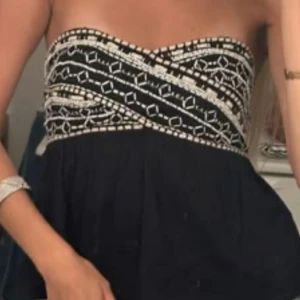 Svart topp från Zara - Elegant svart axelbandslös topp med detaljerat vitt broderi från zara.