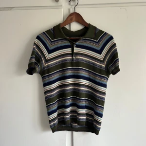 Randig pikétröja från Prada - Säljer en snygg randig pikétröja från Prada i gröna, blå och vita nyanser. I bra skick ända är att Prada loggan har lossnat på ena sidan, går att enkelt sy fast.