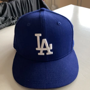 Blå keps från New Era - Säljer en blå keps från New Era med vit broderad logotyp på framsidan. Kepsen är i storlek medium/large och har justerbar passform. Perfekt för att ge din outfit en sportig touch!