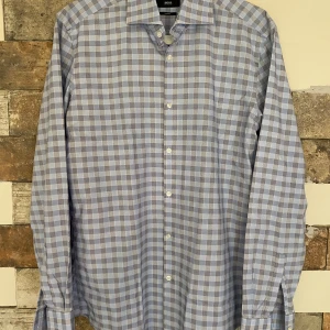 Rutig skjorta från BOSS - Snygg rutig skjorta från BOSS i blå och grå toner. Skjortan har en slim fit passform och är långärmad med klassisk krage och knappar framtill. Perfekt för en stilren look.