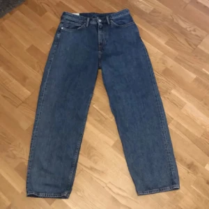 Baggy Jeans - Säljer ett par klassiska blå jeansbyxor med normal passform. De har en traditionell femficksdesign och knappar i midjan. Perfekta för en avslappnad stil.