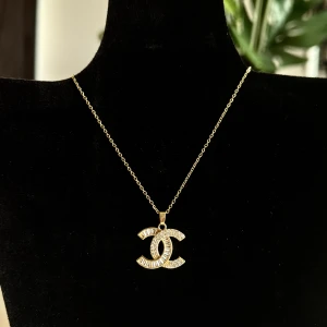 Guldigt halsband - Elegant guldigt halsband. Kedjan är tunn och smidig, vilket ger en stilren look. Berlocken är dekorerad med små stenar som ger en glittrig effekt. Perfekt för att lyfta vilken outfit som helst.