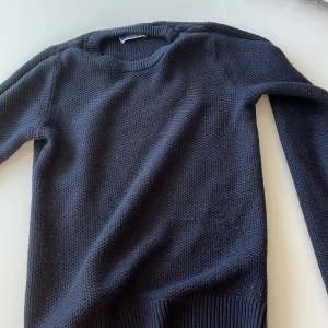 Mörkblå stickad tröja - Säljer en stilren mörkblå stickad tröja med rund halsringning. Tröjan har långa ärmar och ribbade muddar vid ärmslut och nederkant. Perfekt för kyligare dagar!