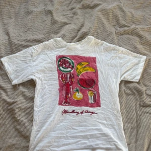 Vit t-shirt från Pull&Bear - Säljer en vit t-shirt från Pull&Bear med ett färgglatt tryck av olika objekt som bananer och drycker. Texten 'Miscellany of things' finns under motivet. Perfekt för en avslappnad stil.