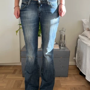Blå bootcut jeans - Snygga blå bootcut jeans med klassisk femficksdesign och knappgylf. Perfekta för en avslappnad stil med en touch av retro. Passar bra till både sneakers och klackar.