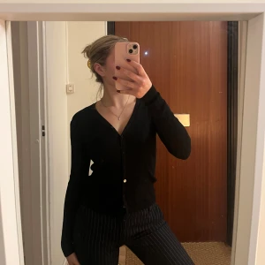 Svart ribbad kofta - Säljer en stilren svart ribbad kofta med knappar framtill. Perfekt för både vardag och mer uppklädda tillfällen. Koftan har en v-ringad design och långa ärmar.