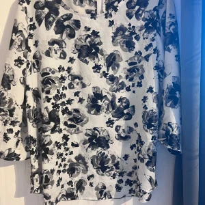 Blommig blus med trekvartsärm - Säljer en stilren blus med svartvita blommönster. Blusen har trekvartsärmar och en rund halsringning. Perfekt för en chic look.