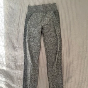 Grå leggings från Gymshark - Snygga grå leggings från Gymshark med hög midja och elastiskt material. Perfekta för träning med en bekväm passform och stilren design. Gymshark-loggan i blått på baksidan av midjan ger en cool touch. Säljer för 150kr + frakt 