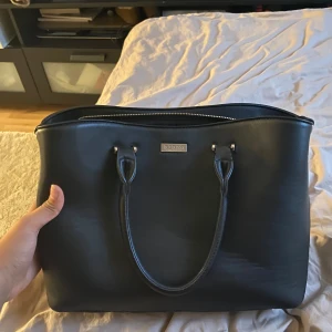 Handväska  - Snygg svart handväska  med dragkedja upptill. Väskan har två handtag och en stilren design, perfekt för att bära dina dagliga nödvändigheter. Insidan har flera fack för enkel organisering. Classy och så snygg, funkar perfekt för skolan. Man får plats med dator i den som är så bra!