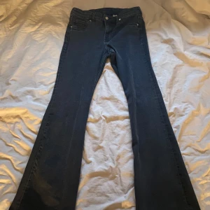 Lågmidjade svarta jeans  - Snygga mörkblå jeans från Divided i storlek 42. De har en klassisk design med fem fickor och en knappgylf. Perfekta för en avslappnad stil. Låg midjade, passar nån som är 170+. Är strl 42 men passar 40/38! Säljer ett par blå i samma storlek och allt!