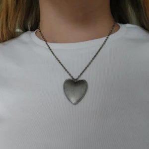 Halsband med hjärtformat hänge - Snyggt halsband i silverfärg med ett hjärtformat hänge. Kedjan är tunn och elegant, perfekt för att ge en subtil touch till din outfit. Hjärtat är enkelt och stilrent, vilket gör det lätt att matcha med andra smycken.🩶