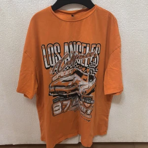Orange t-shirt med tryck från Shein - Cool orange t-shirt från Shein med ett stort tryck av en bil och texten 'Los Angeles California Speed'. Perfekt för en avslappnad stil med en touch av racingkänsla. Kortärmad och i mjukt material.