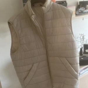 Beige quiltad väst från Zara - Säljer en stilren beige quiltad väst från Zara. Västen har en dragkedja framtill och är perfekt för lager-på-lager under kyligare dagar. Den har en klassisk design med en modern touch. Nypris låg runt 800, mitt pris 300. 