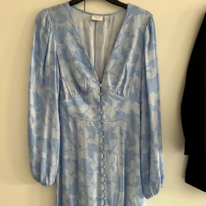 Blå blommig klänning från VILA - Klänning från NA-KD med blommigt mönster och v-ringning. Klänningen har långa ärmar och knappar framtill. Luftigt och skönt material. Använd 1 gång, nypris 799kr. Storlek xs/34 men passar S! 