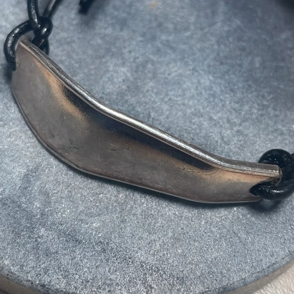 Snyggt armband med en bred silverfärgad platta och justerbart svart band. Perfekt för en stilren look.. Asusteet.