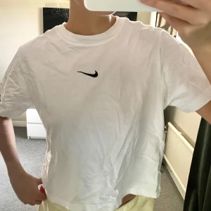 Vit t-shirt från Nike - Säljer en klassisk vit t-shirt från Nike med deras ikoniska logga på bröstet. T-shirten har en normal passform och är kortärmad