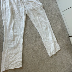 Vita linnebyxor från Roxy - Säljer ett par vita linnebyxor från Roxy i storlek M. Byxorna har en avslappnad passform med elastisk midja och snörning. Perfekta för varma dagar med sin lätta och luftiga känsla. De har praktiska fickor både fram och bak.