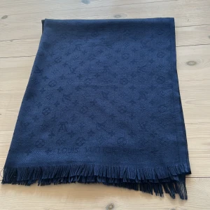 Louis Vuitton halsduk - Elegant mörkblå halsduk från Louis Vuitton med diskret mönster och fransar i kanterna. Perfekt för att ge en lyxig touch till din outfit. Den är otroligt mjuk och skön att ha på sig. Tvärr har jag tappat bort LV boxen. 