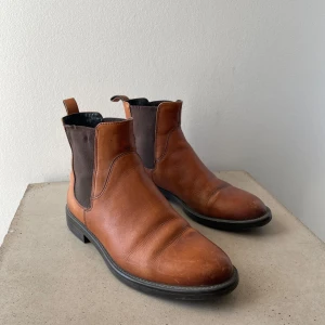 Bruna Chelsea boots från Vagabond - Snygga bruna Chelsea boots från Vagabond i skinn. De har en elastisk panel på sidan för enkel på- och avtagning samt en låg klack. Perfekta för en stilren look. Storlek: 36